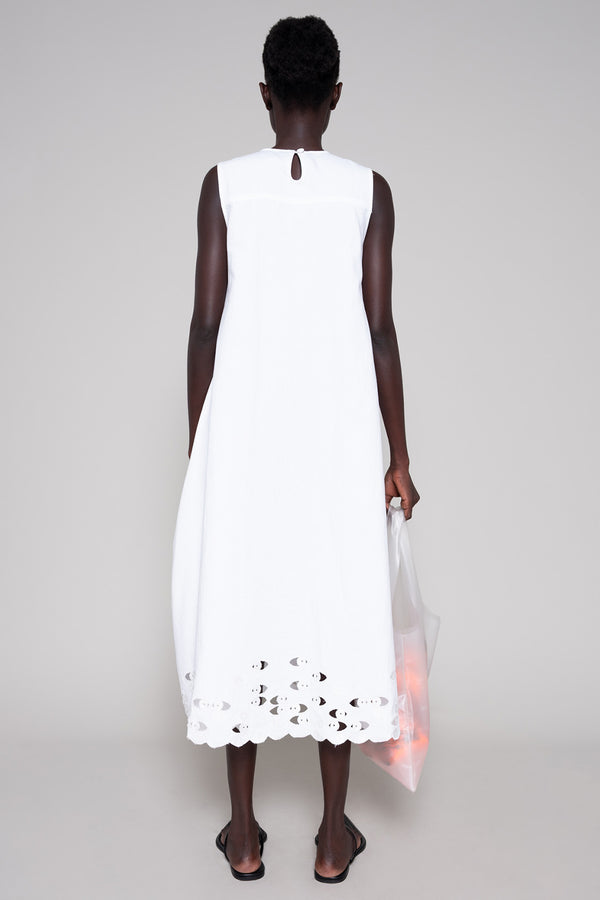 Person wearing white sleeveless dress with a tote bag on plain background
