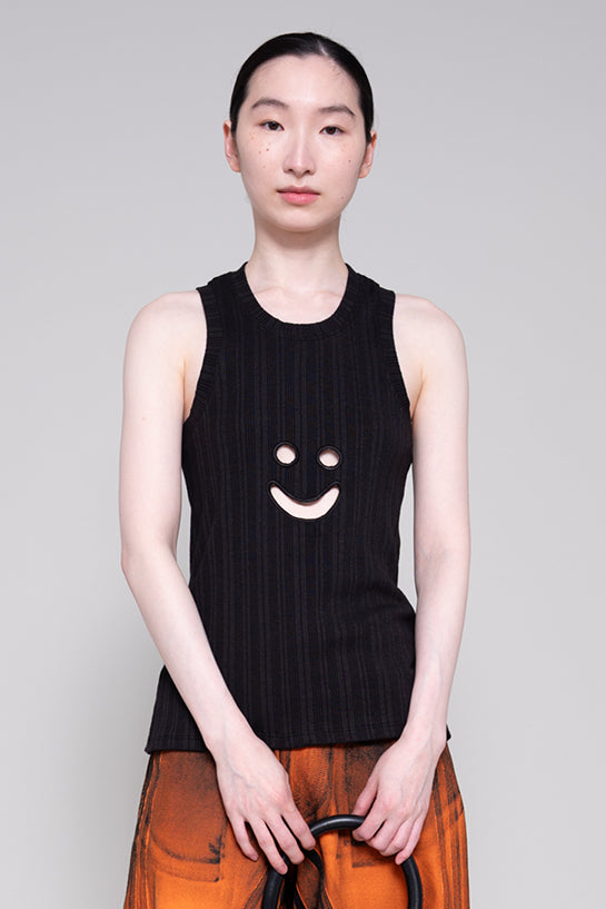 Person wearing a black sleeveless top with a smiley face design on a plain background