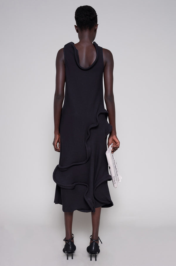 Person wearing a black dress and heels holding a tote bag on a plain background