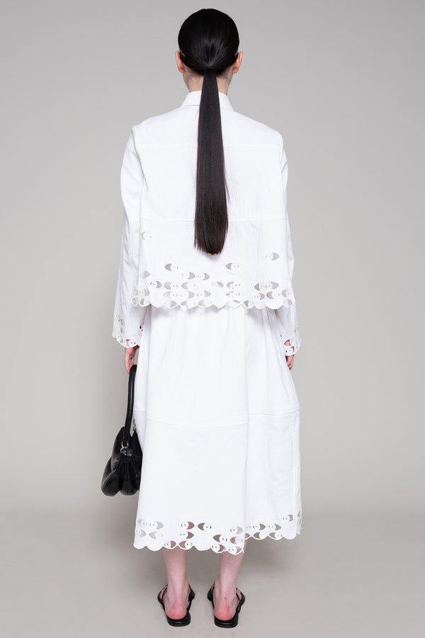 Person wearing a white shirt and skirt with cut-out details on a plain background