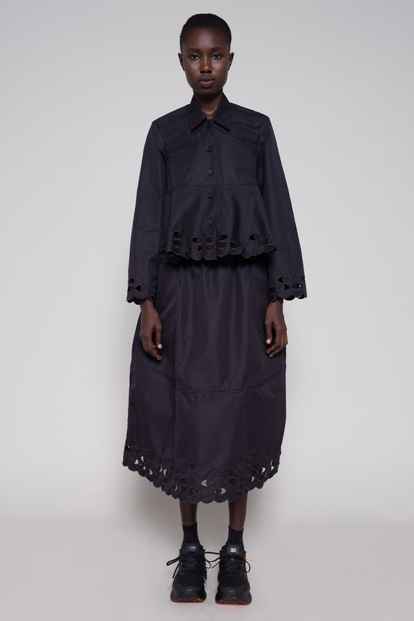 Person wearing a black shirt and skirt with cut-out details on a plain background