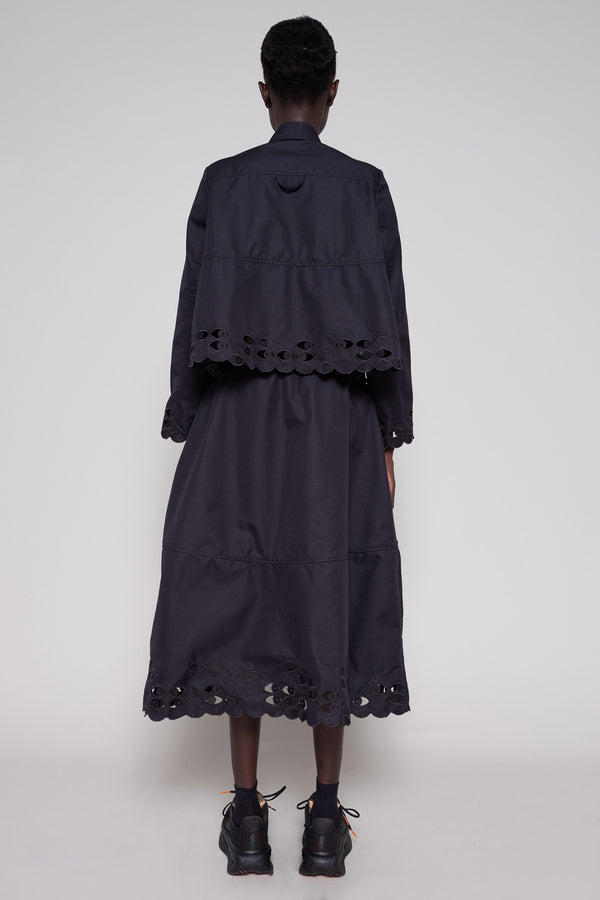 Person wearing a black shirt and skirt with cut-out details on a plain background