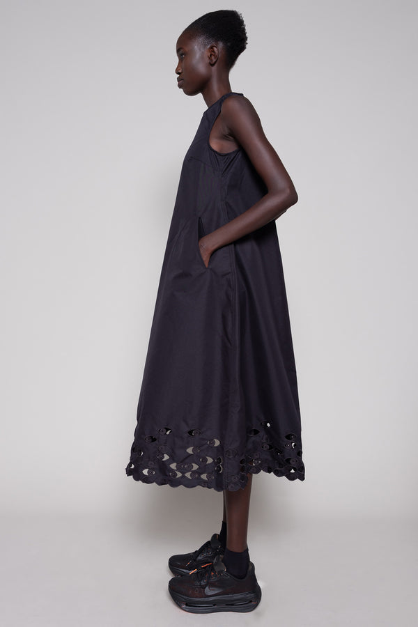 Person wearing a black sleeveless dress with cut-out details on a plain background