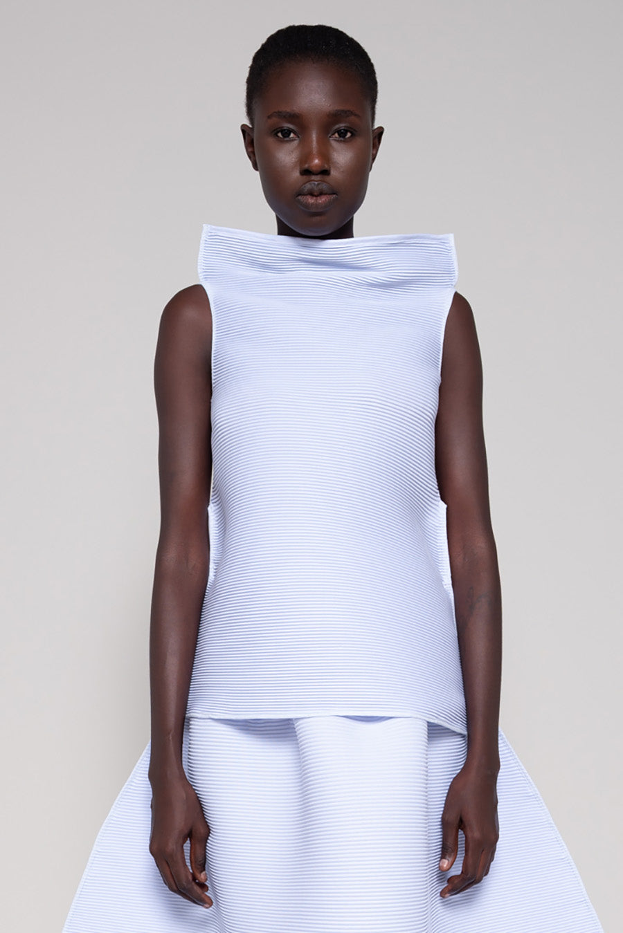 Person wearing a light blue sleeveless top with a high neckline on a plain background