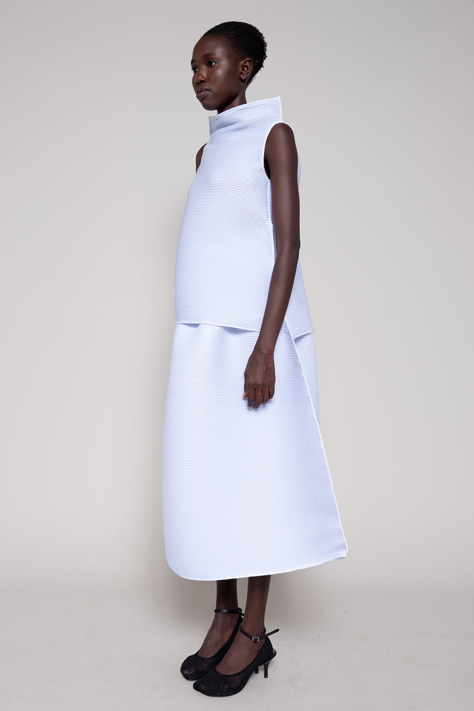 Woman wearing a white sleeveless dress against a plain background