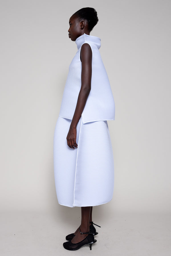 Woman wearing a white sleeveless top and skirt set on a plain background