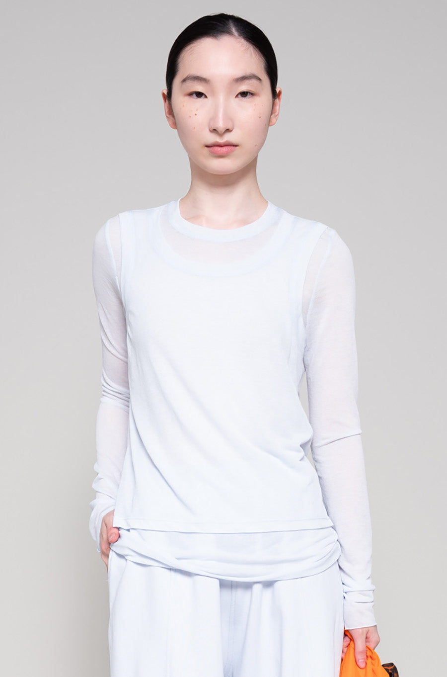 Person wearing light long-sleeve top and light-colored pants, holding an orange tote bag on a plain background