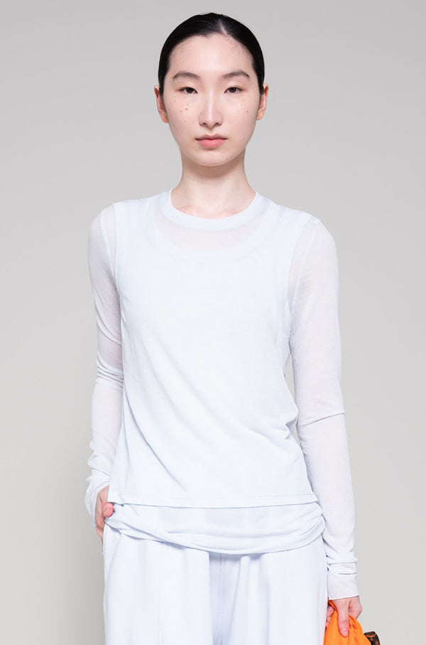 Person wearing light long-sleeve top and light-colored pants, holding an orange tote bag on a plain background