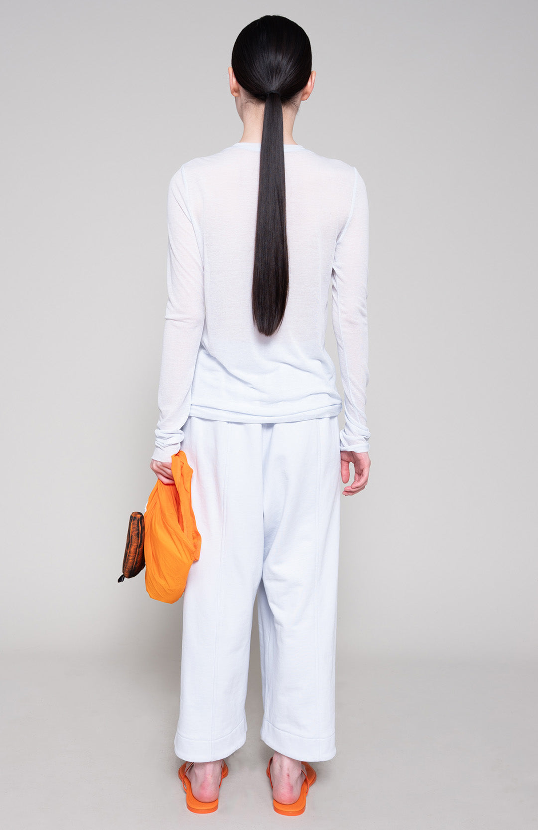 Person wearing a matching long sleeve and sweatpants holding an orange bag on a plain background