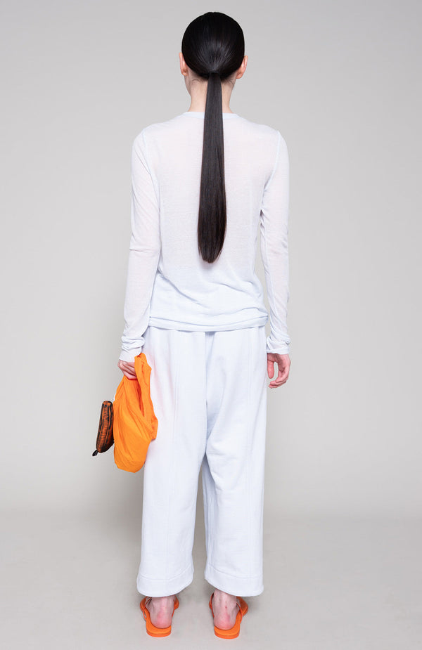 Person wearing a matching long sleeve and sweatpants holding an orange bag on a plain background