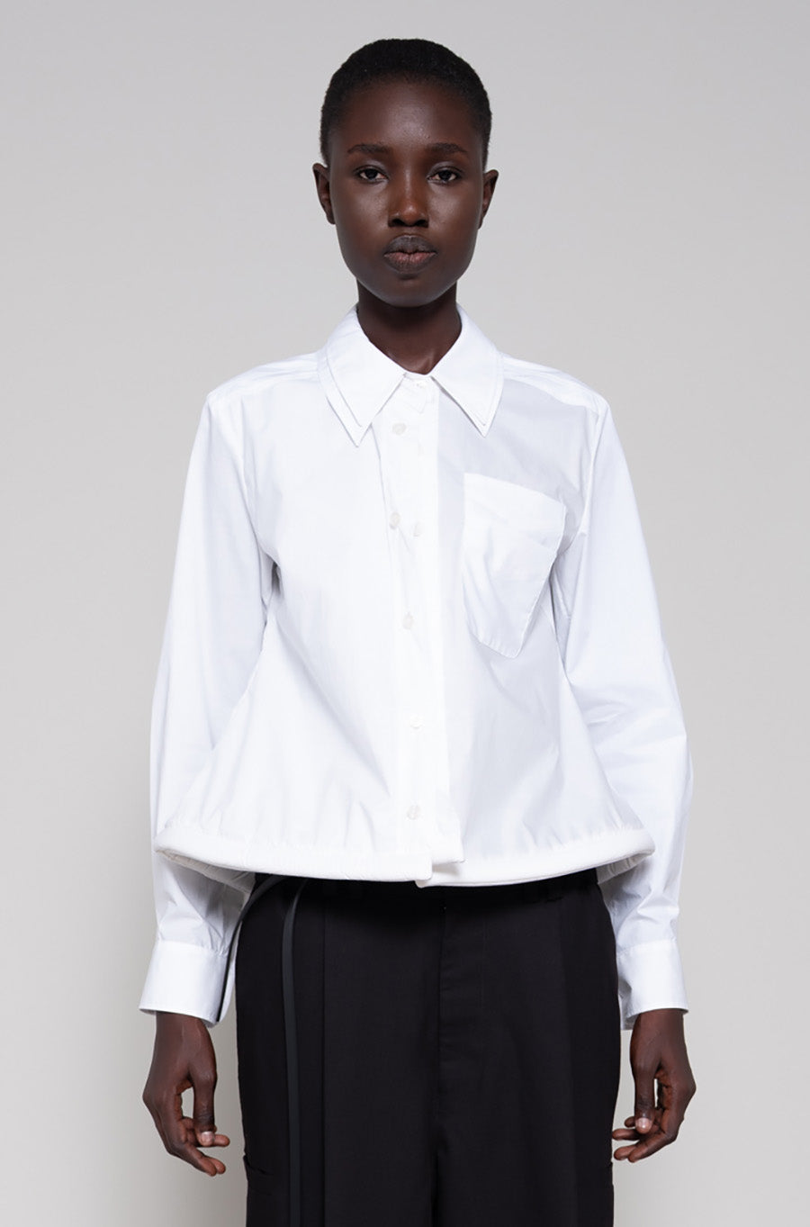 Person wearing a white shirt and black pants against a plain background