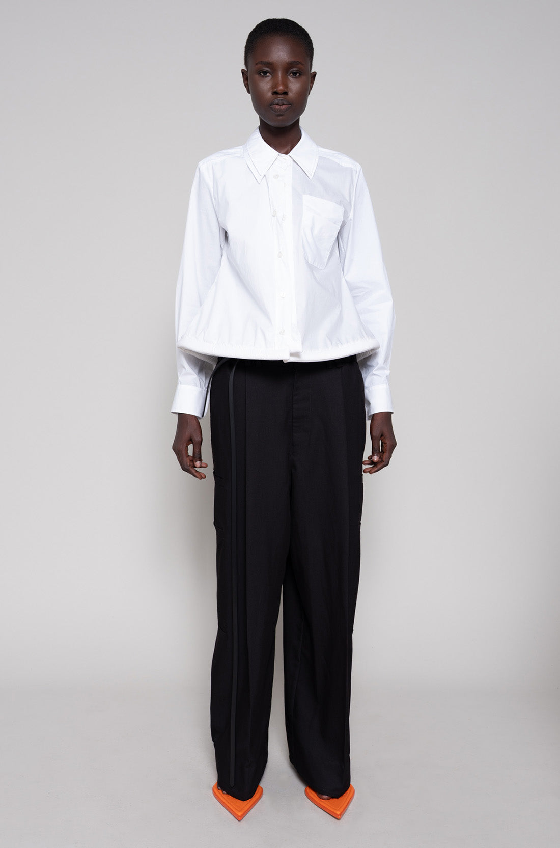 Person wearing a white shirt, black pants and orange flip flops on a plain background