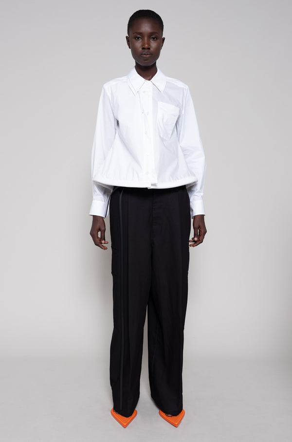 Person wearing a white shirt, black pants and orange flip flops on a plain background