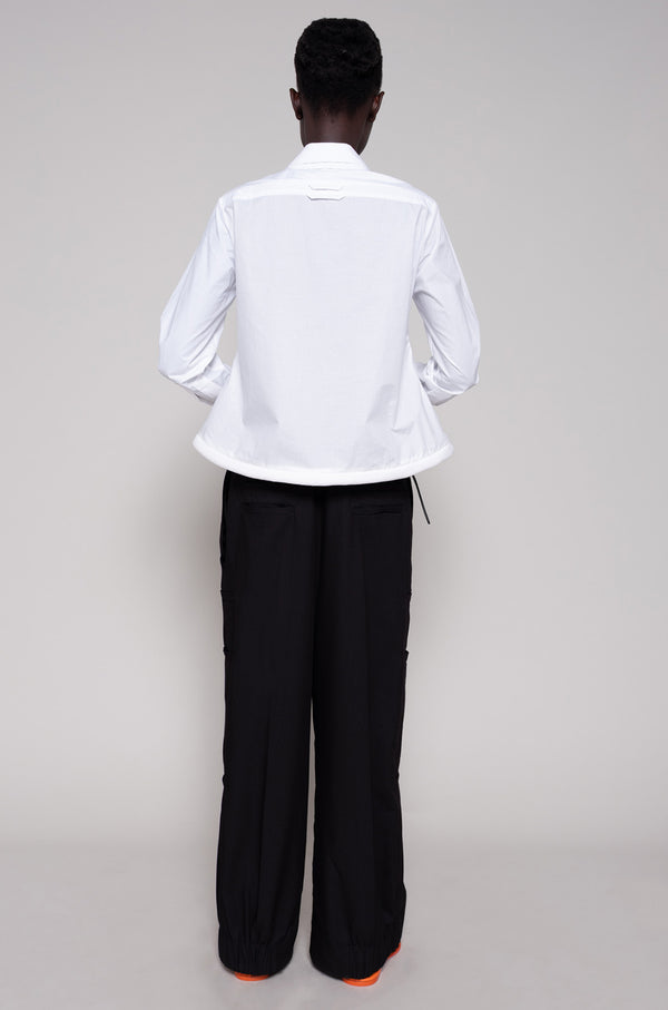 Person wearing a white shirt and black pants on a plain background
