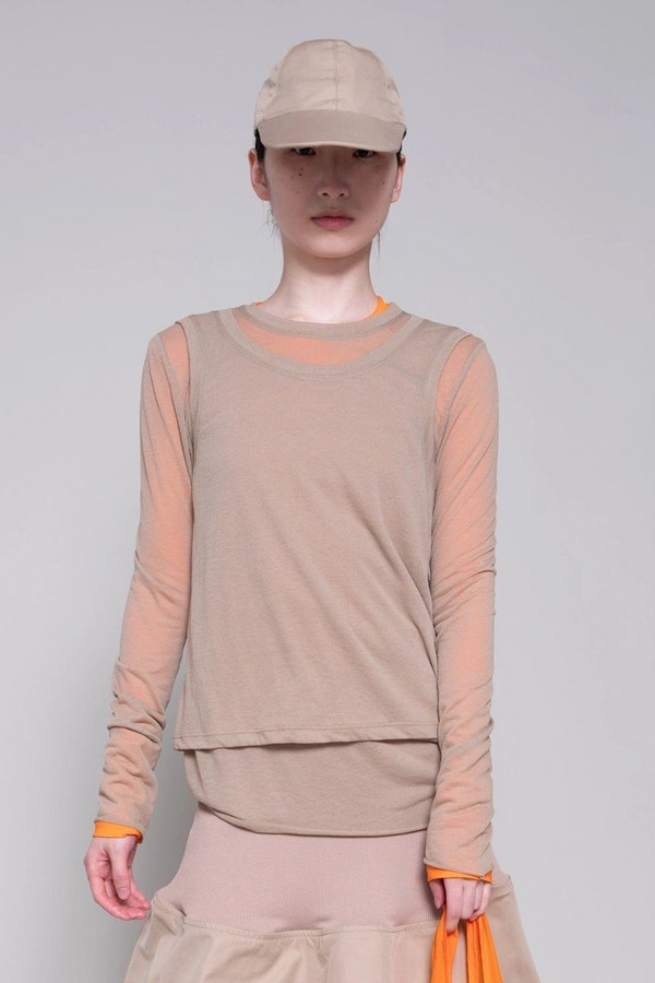 Person wearing a beige long-sleeve top and cap on a plain background