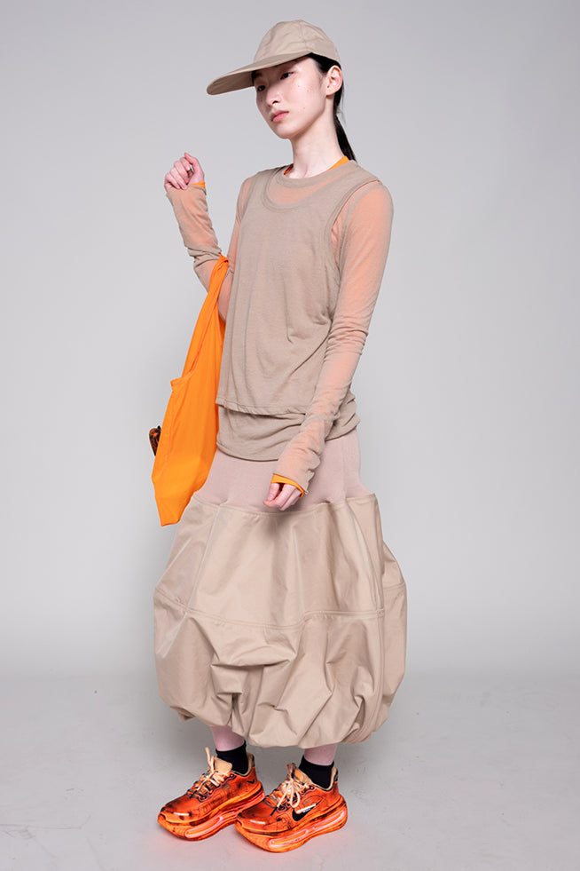 Person wearing a beige outfit with orange shoes and an orange bag on a gray background