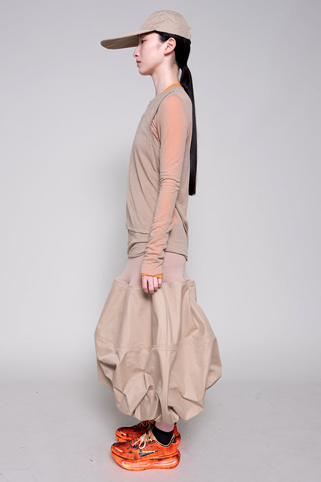 Person wearing a beige outfit with orange shoes on a plain background