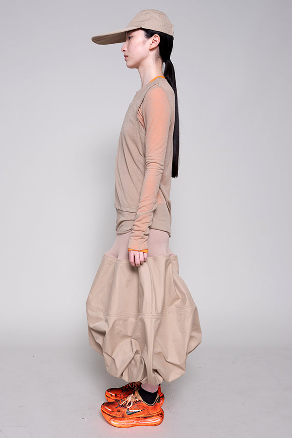Person wearing a beige outfit with orange shoes on a plain background