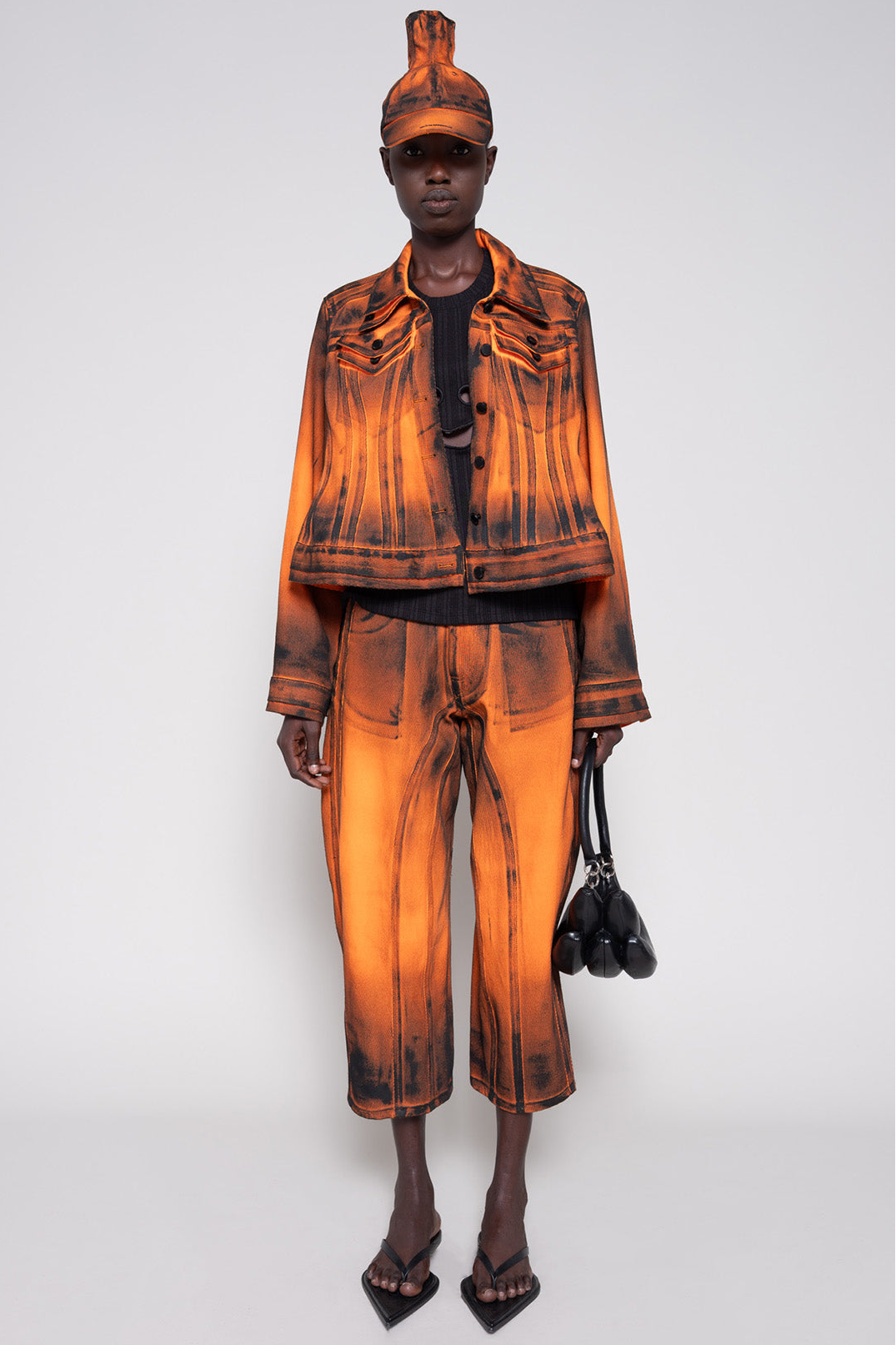 Model front full wearing an orange denim set that's hand-painted black at the seams for a shadow 3-D effect.