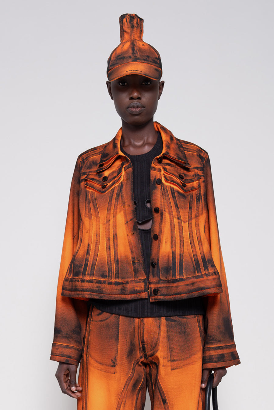 Model wearing an orange denim set that's hand-painted black at the seams for a shadow 3-D effect.