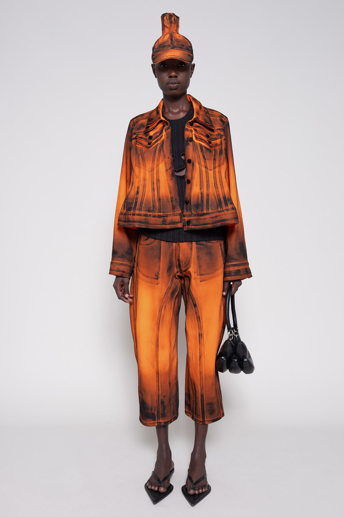 Model front full wearing an orange denim set that's hand-painted black at the seams for a shadow 3-D effect.