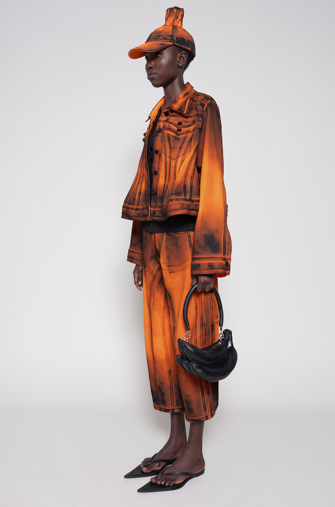 Model side full wearing an orange denim set that's hand-painted black at the seams for a shadow 3-D effect.