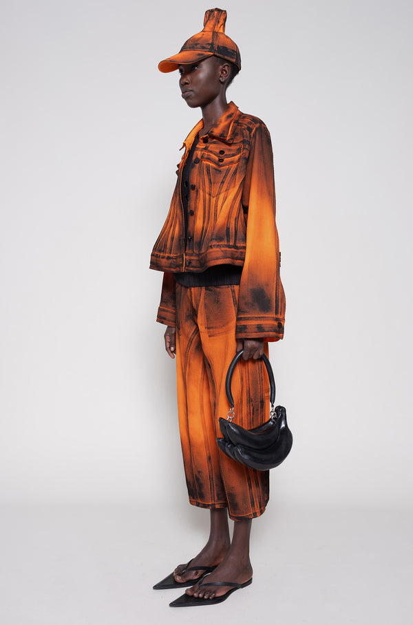 Model side full wearing an orange denim set that's hand-painted black at the seams for a shadow 3-D effect.