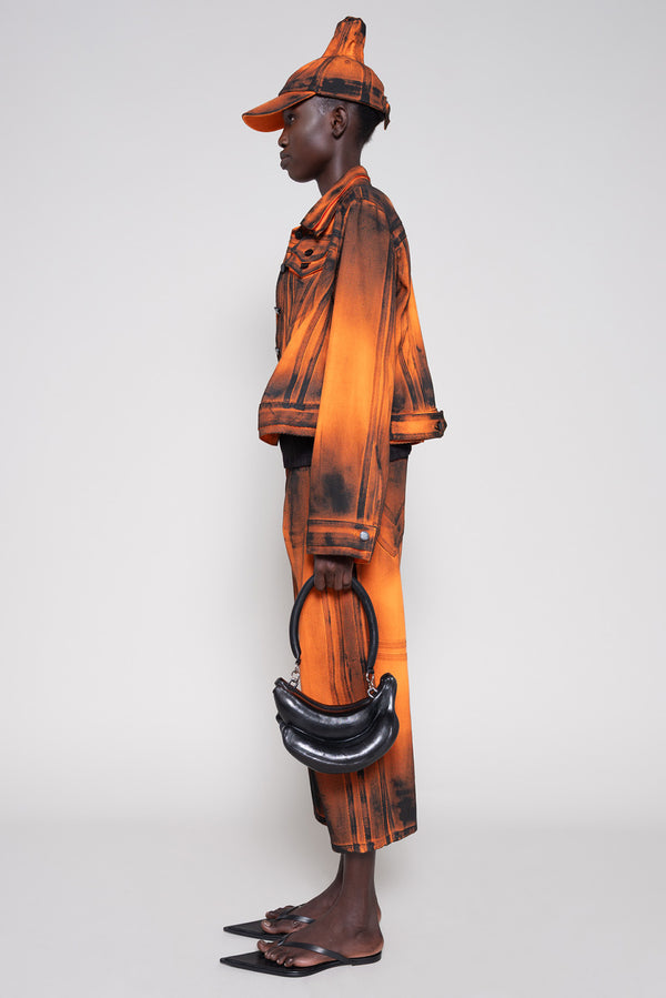 Model side full wearing an orange denim set that's hand-painted black at the seams for a shadow 3-D effect.