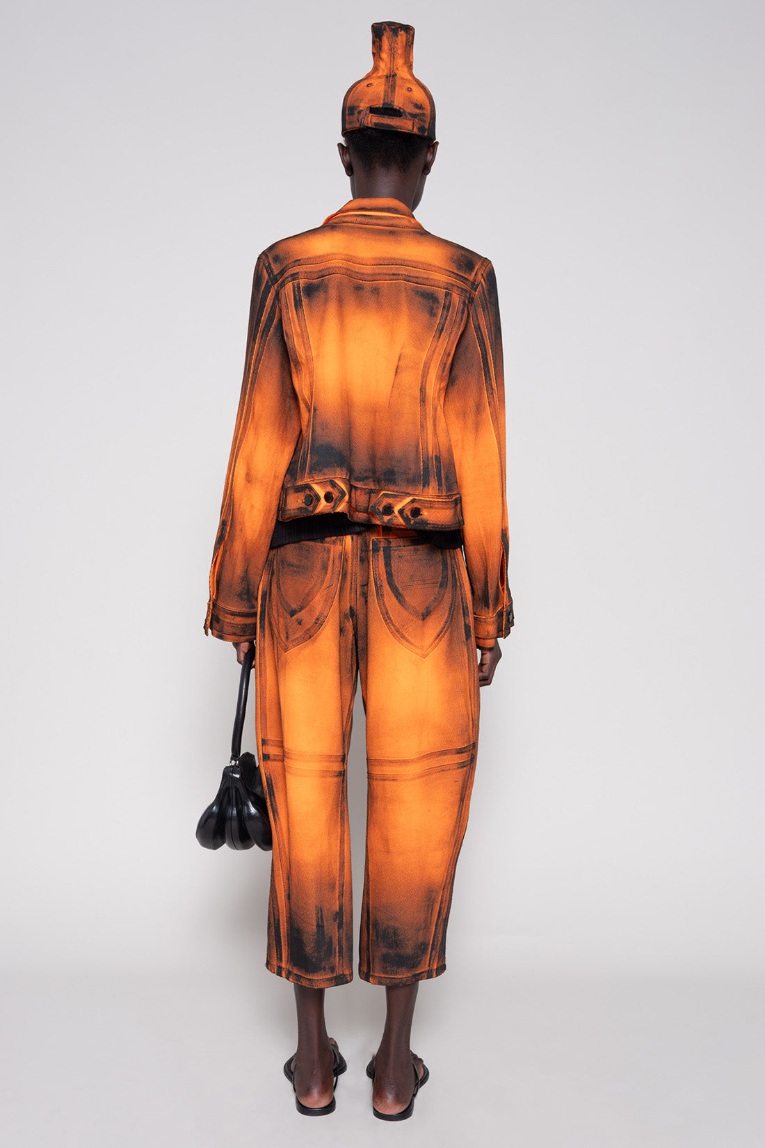 Model back full wearing an orange denim set that's hand-painted black at the seams for a shadow 3-D effect.