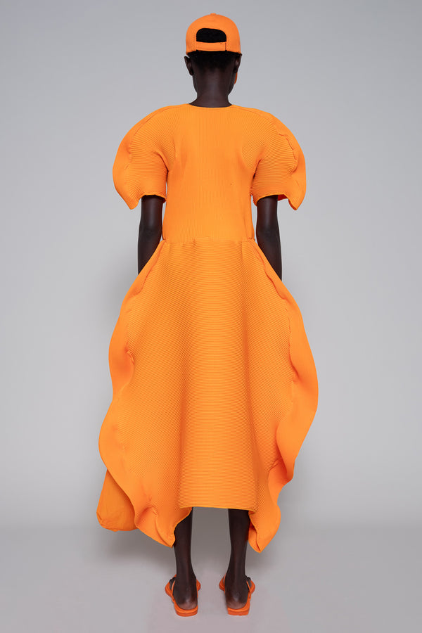 Person wearing an orange dress, tote bag, flip flops and cap on a gray background