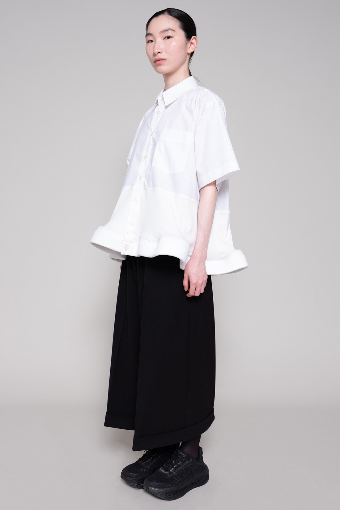 Person wearing a white shirt and black pants on a plain background