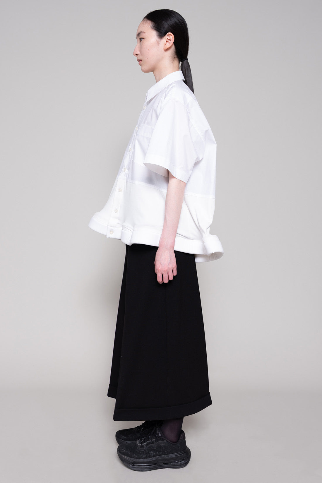 Person wearing a white shirt and black pants on a plain background