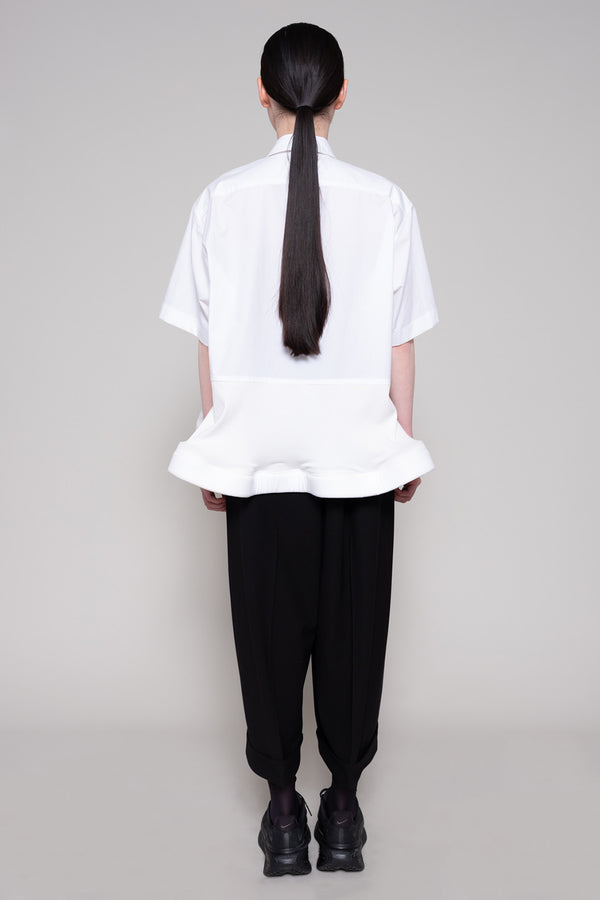 Person wearing a white shirt and black pants on a plain background