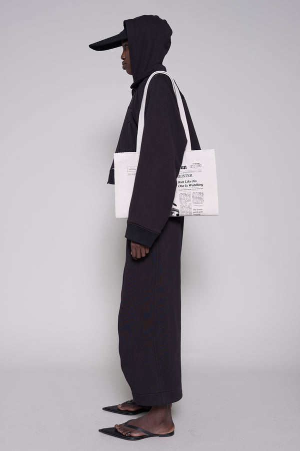 Person wearing a black outfit with a white tote bag on a gray background