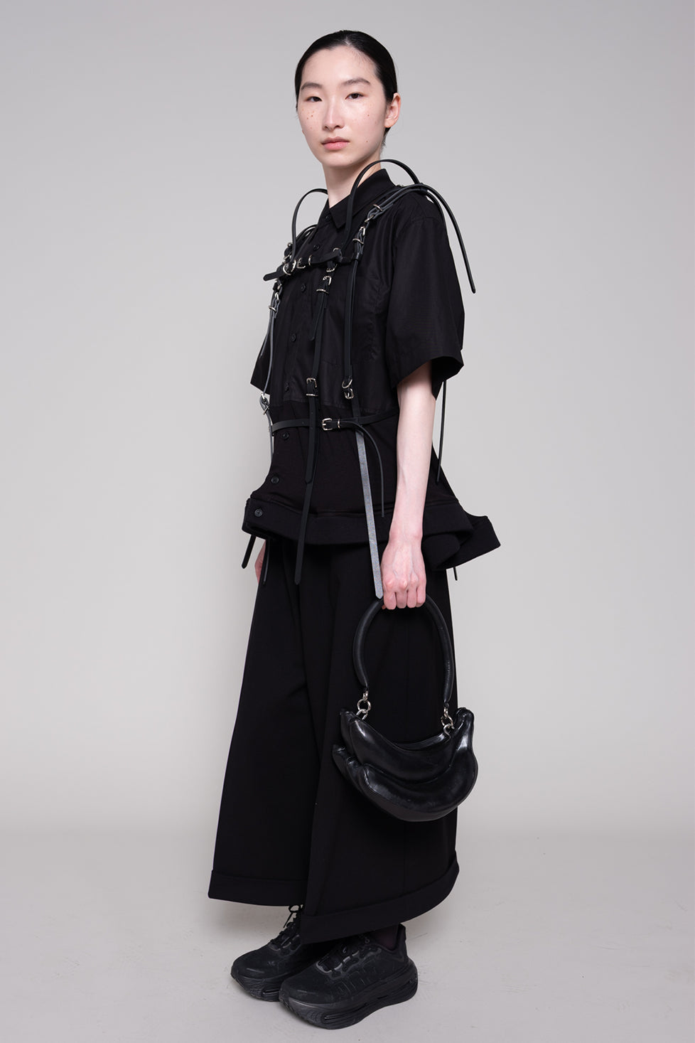 Person wearing a black outfit with a bag on a gray background