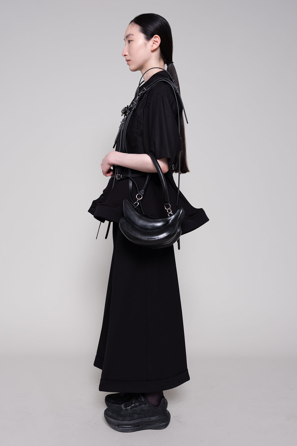 Person wearing a black outfit with a handbag on a plain background