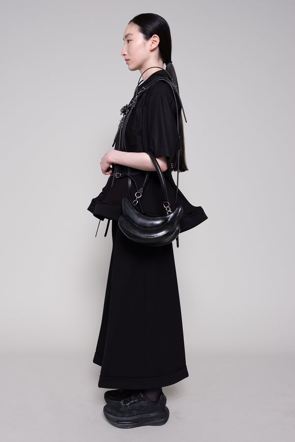 Person wearing a black outfit with a handbag on a plain background