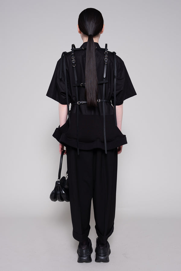Person wearing a black outfit with suspenders on a plain background