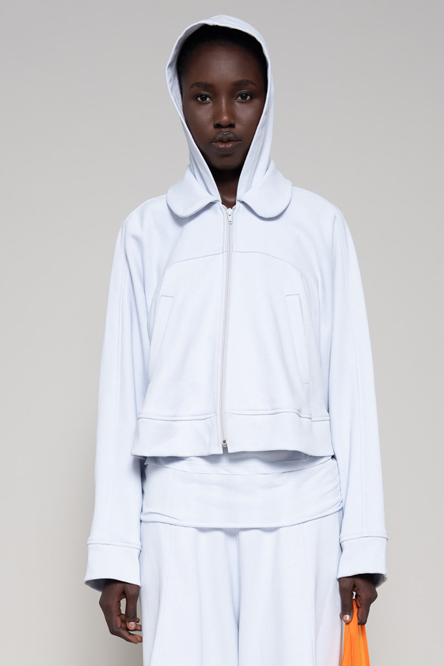 Person wearing a light blue hoodie and sweatpants  with  an orange bag on a plain background