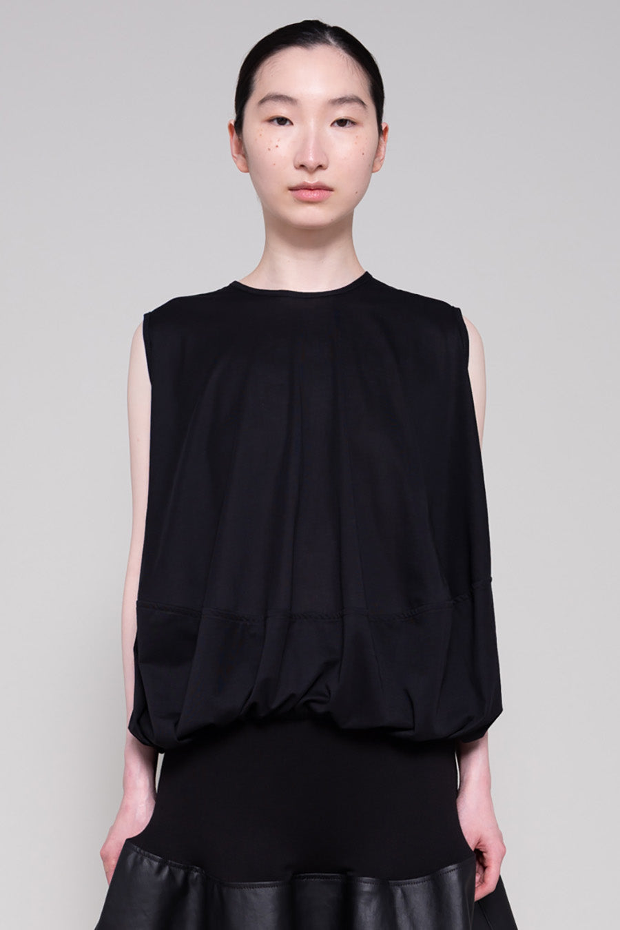 Person wearing a black sleeveless top and black leather skirt on a plain background