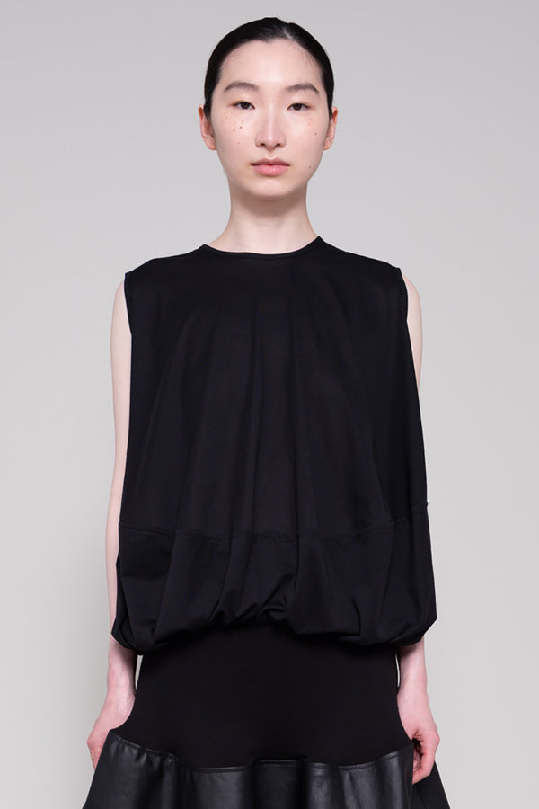Person wearing a black sleeveless top and black leather skirt on a plain background