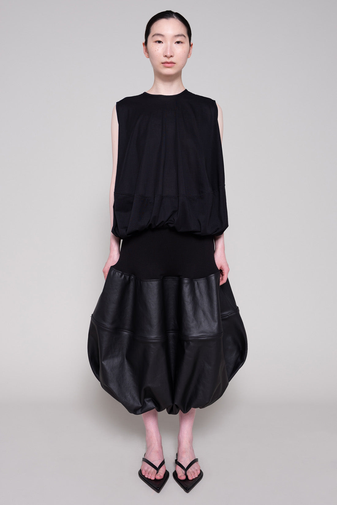Person wearing a black sleeveless top and black leather skirt on a plain background