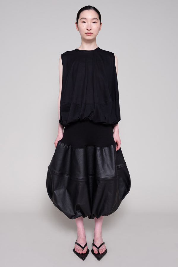 Person wearing a black sleeveless top and black leather skirt on a plain background