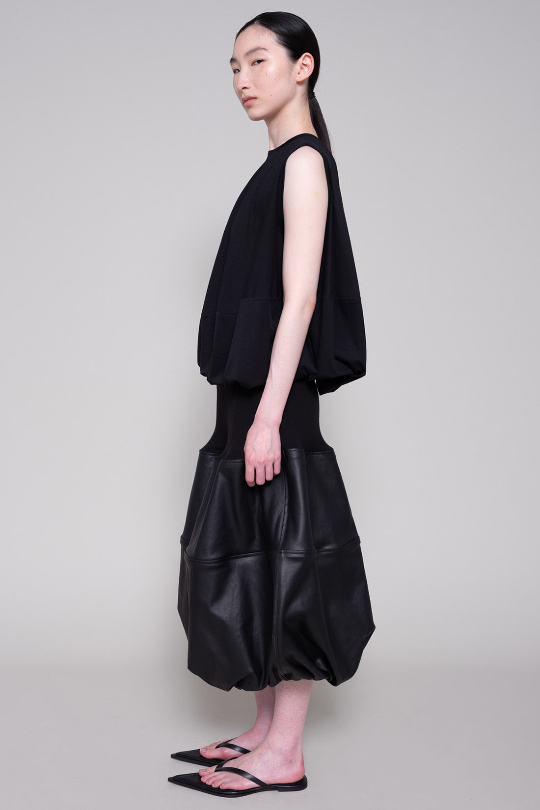 Person wearing a black sleeveless top and black leather skirt on a plain background