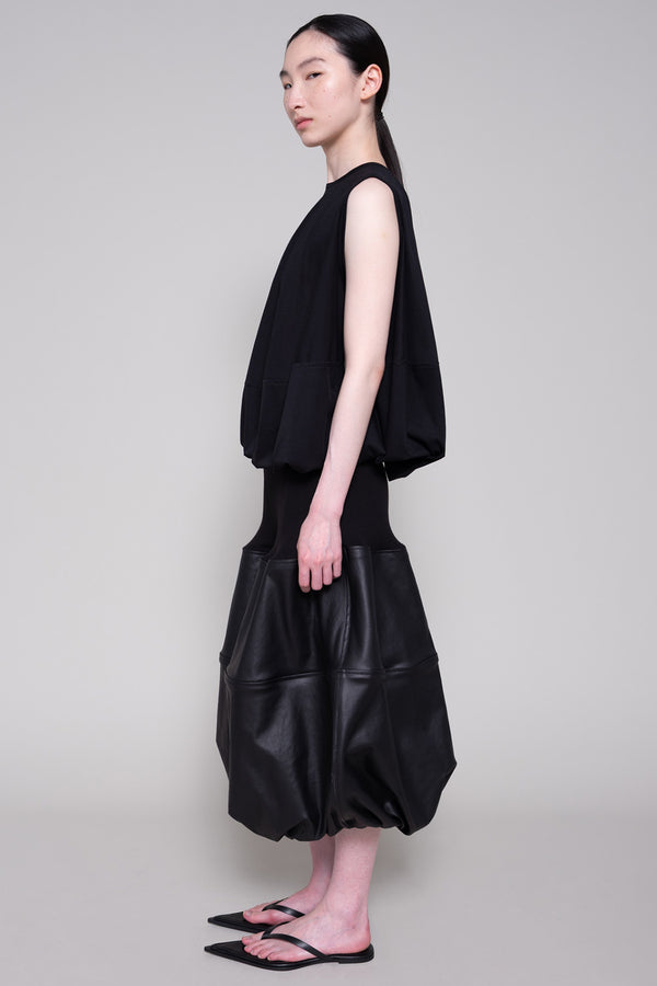 Person wearing a black sleeveless top and black leather skirt on a plain background