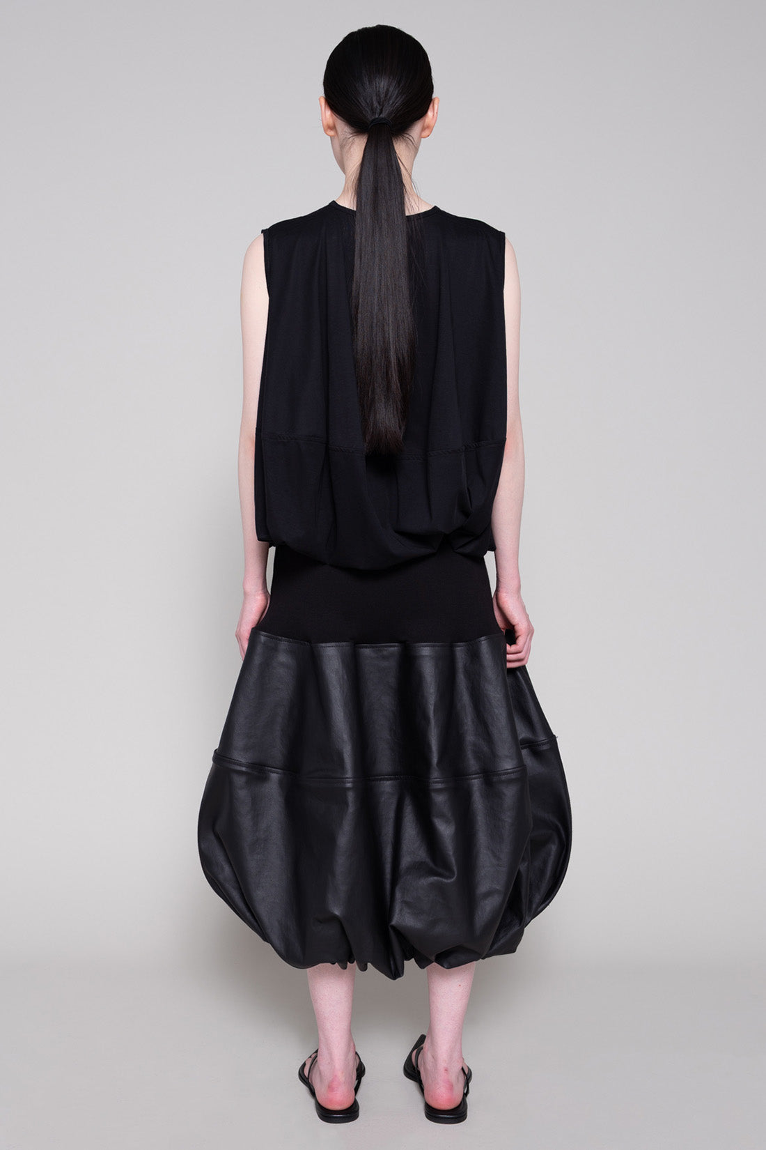 Person wearing a black sleeveless top and black leather skirt on a plain background