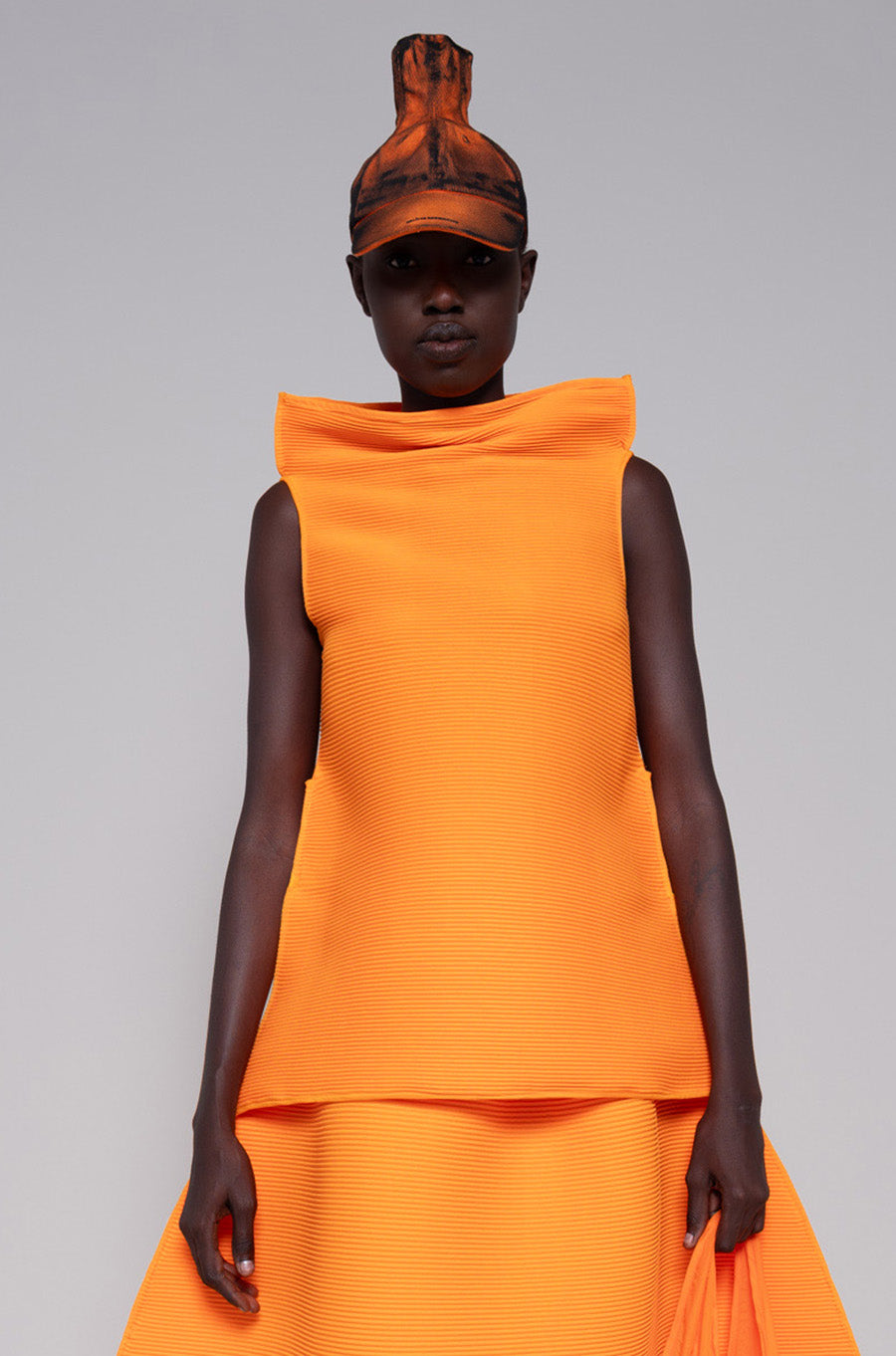 Person wearing a orange sleeveless top and skirt with painted hat and tote bag against plain background