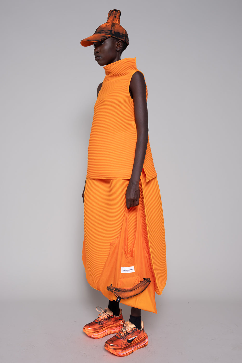 Person wearing an orange outfit with a matching cap on a gray background