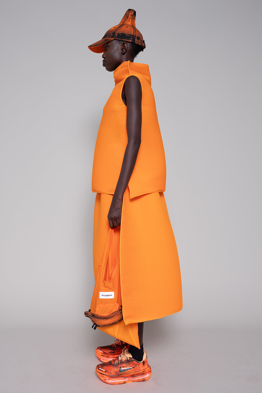 Person wearing an orange outfit with a matching hat on a gray background