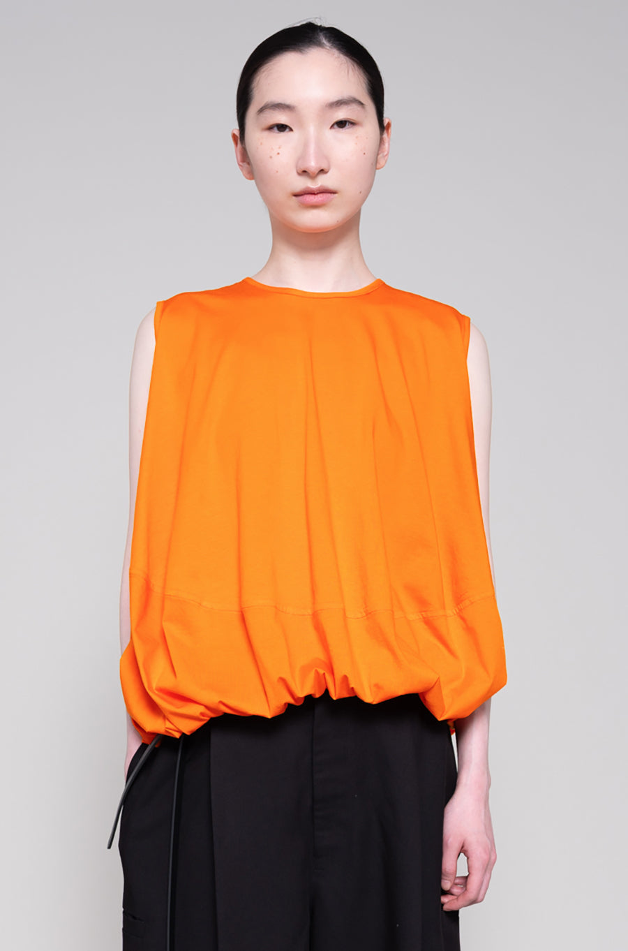 Person wearing an orange sleeveless top and black pants on a plain background